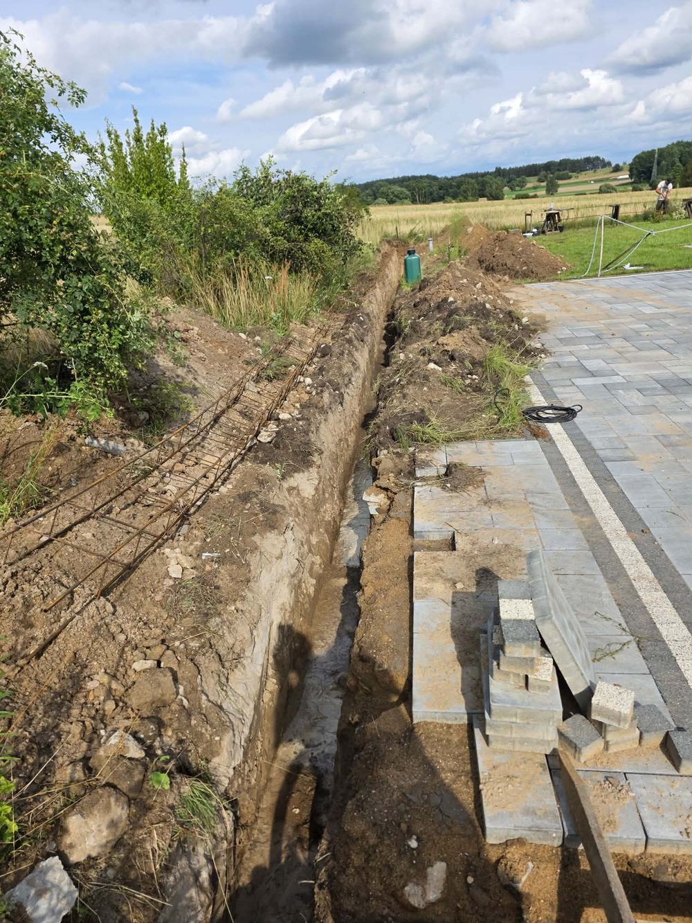 Wykop pod podmurówkę ogrodzenia z przygotowanym zbrojeniem, przy ułożonej kostce brukowej
